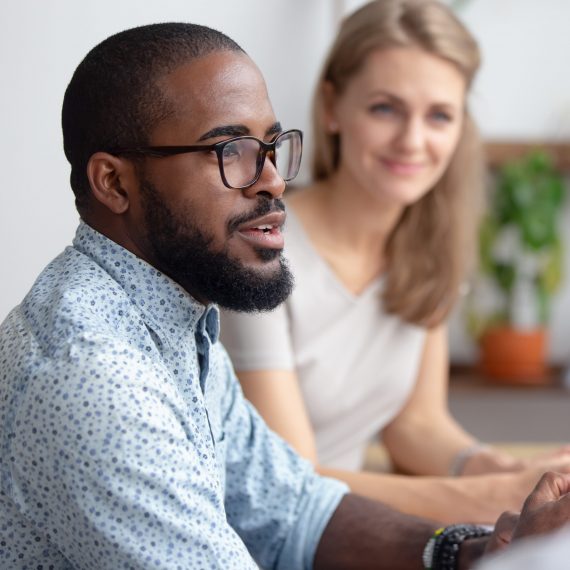 Excited male african-american talking to coworkers timeout in office informal partners conversation. Black manager telling interesting story, sharing news, business strategy. Blur background